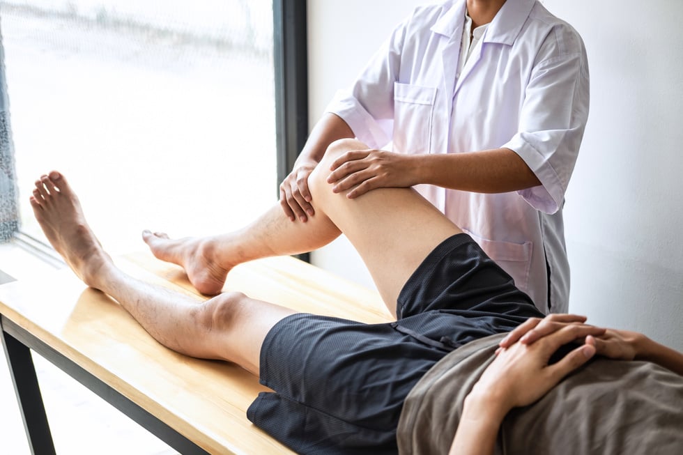 Female Physiotherapist Working Treating a Man's Injured Leg 